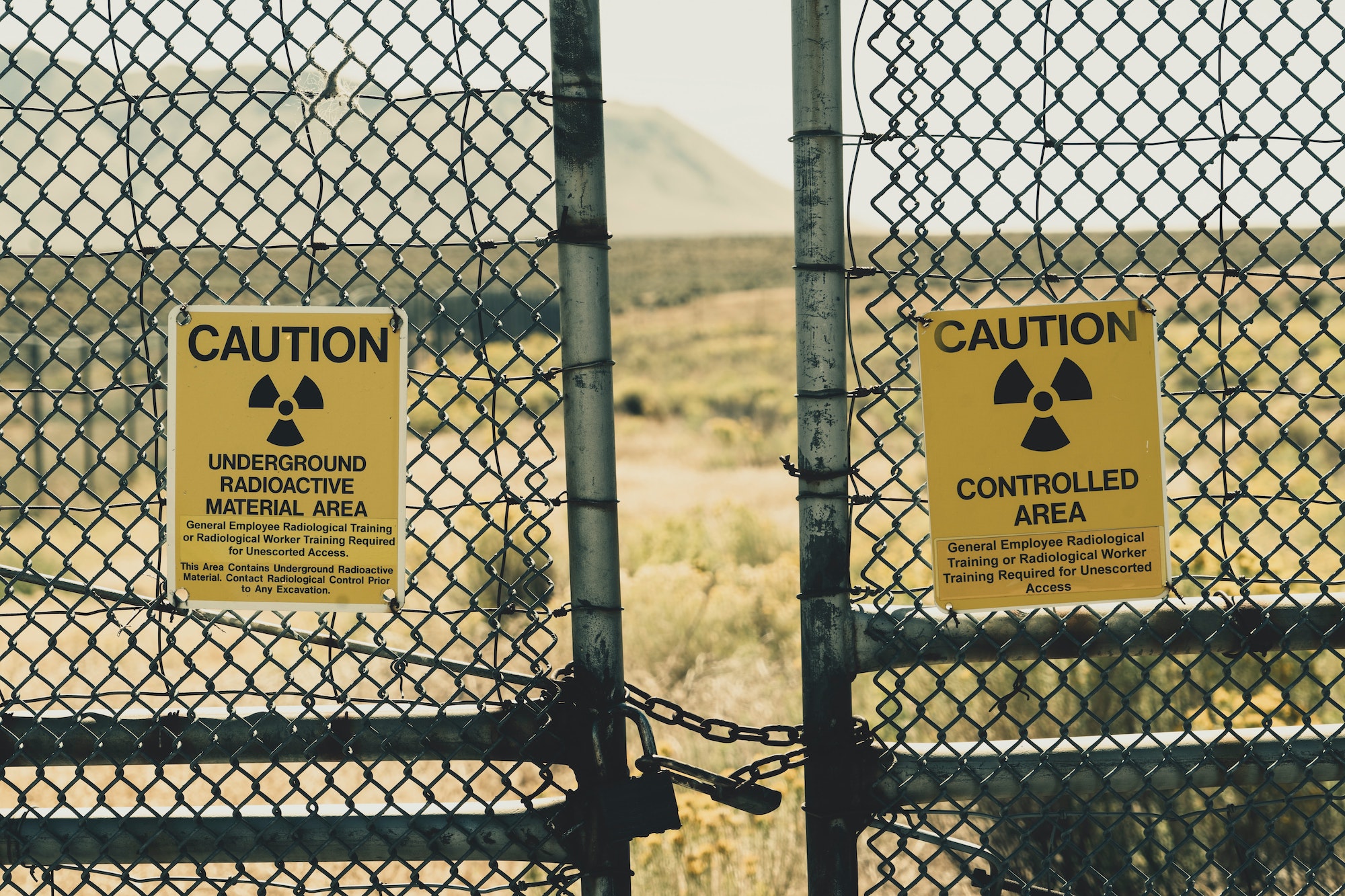 a metal fence gate with signs attached on each side bearing the nuclear energy icon and a warning that reads “underground radioactive material area"