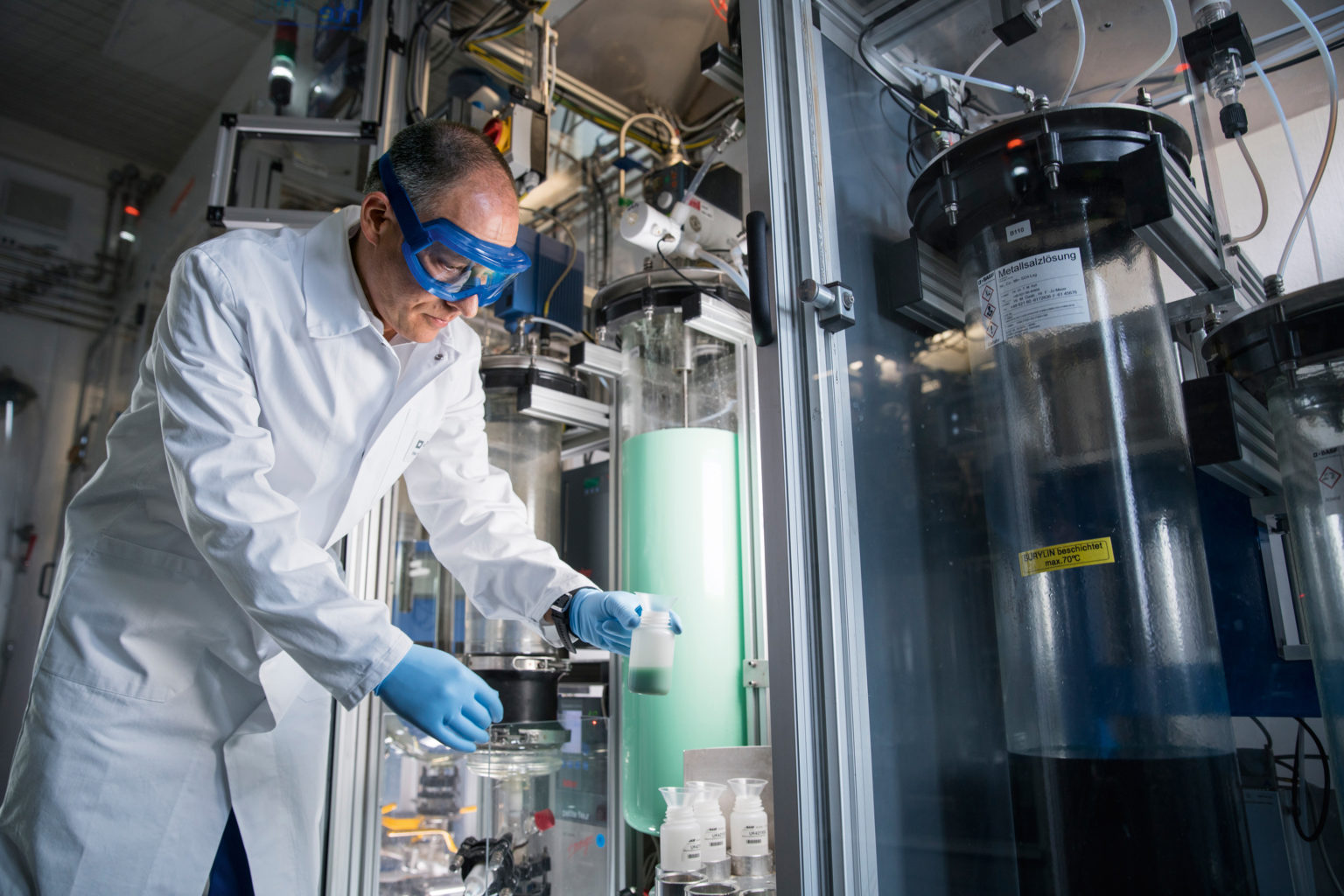 Man in lab coat and goggles holding a glass of green liquid in a BASF chemicals facility
