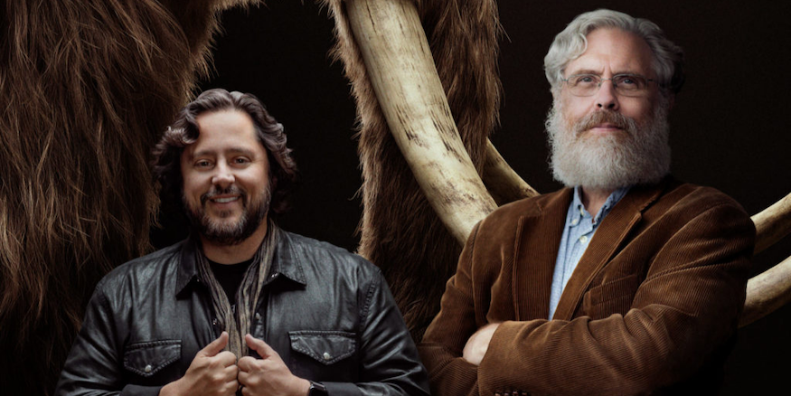 Ben Lamm and George Church standing in front of a cropped image of a woolly mammoth