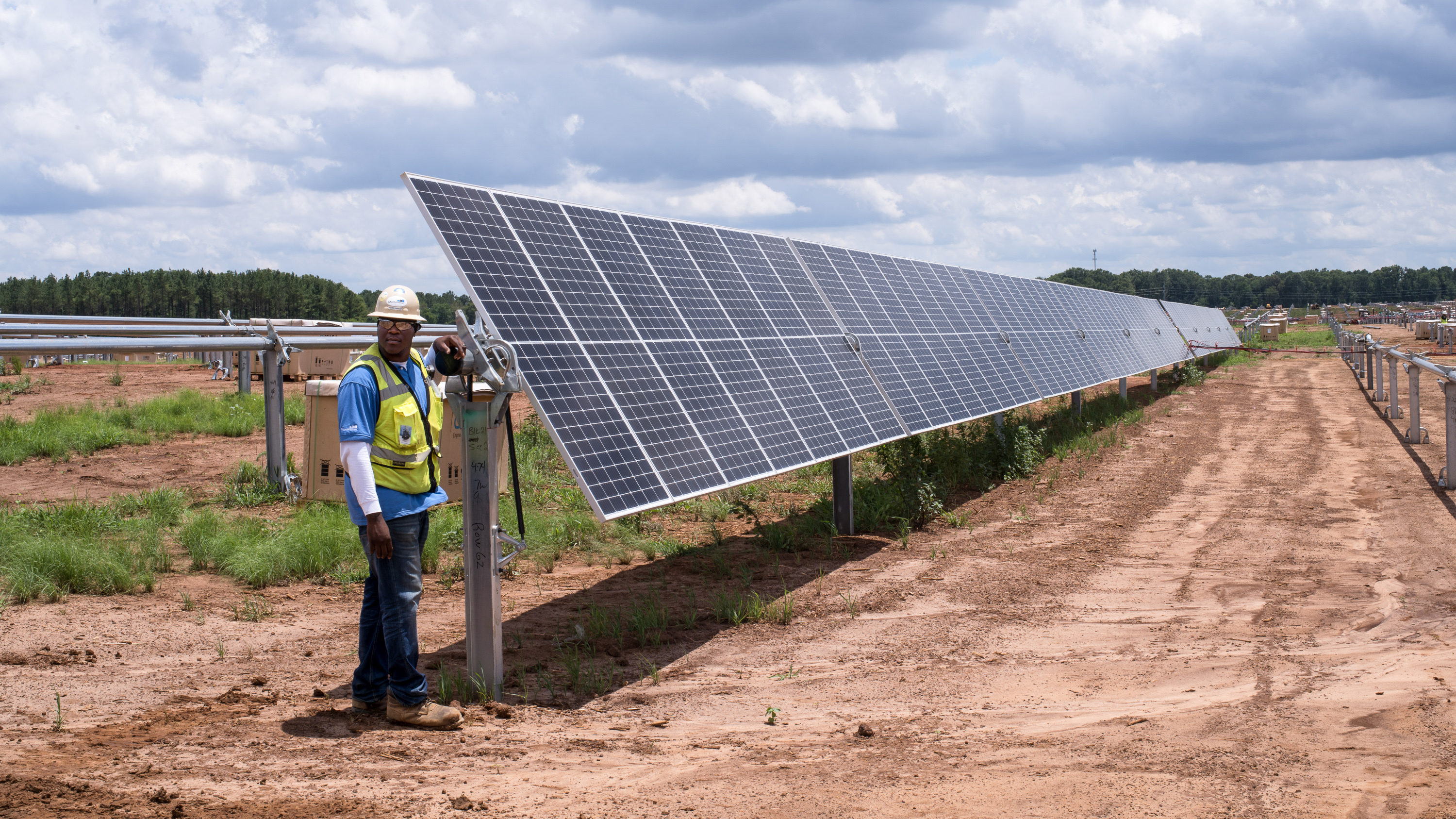 Man in protective gear standing in front of a row of solar modules fixed on the ground