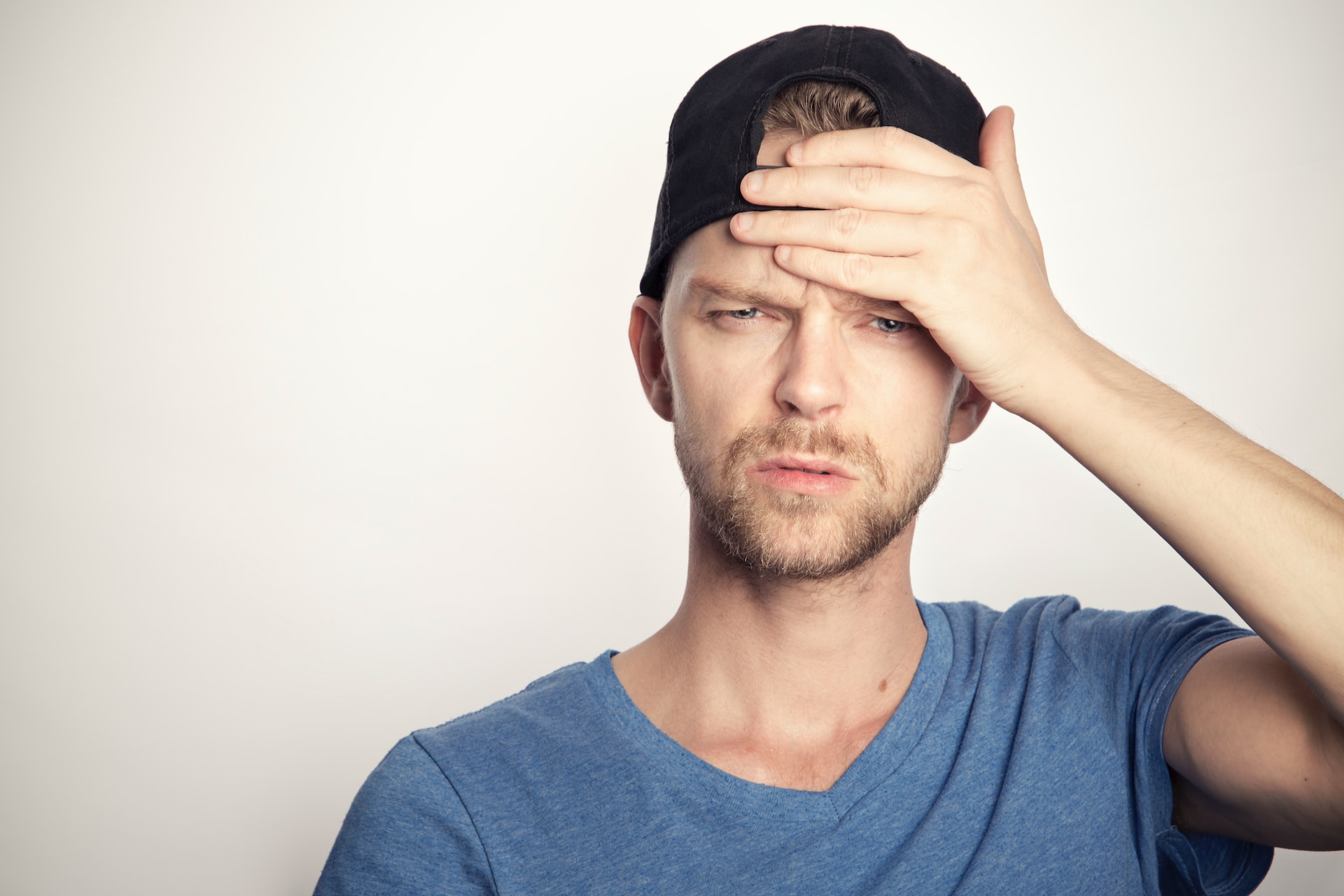 Confused man in baseball cap with hand on forehead