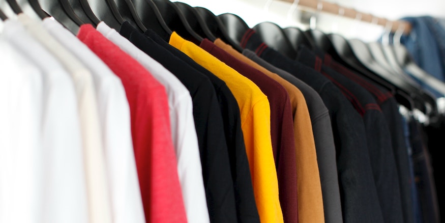 t-shirts and sweaters of varying colours hanging on a coatrack 