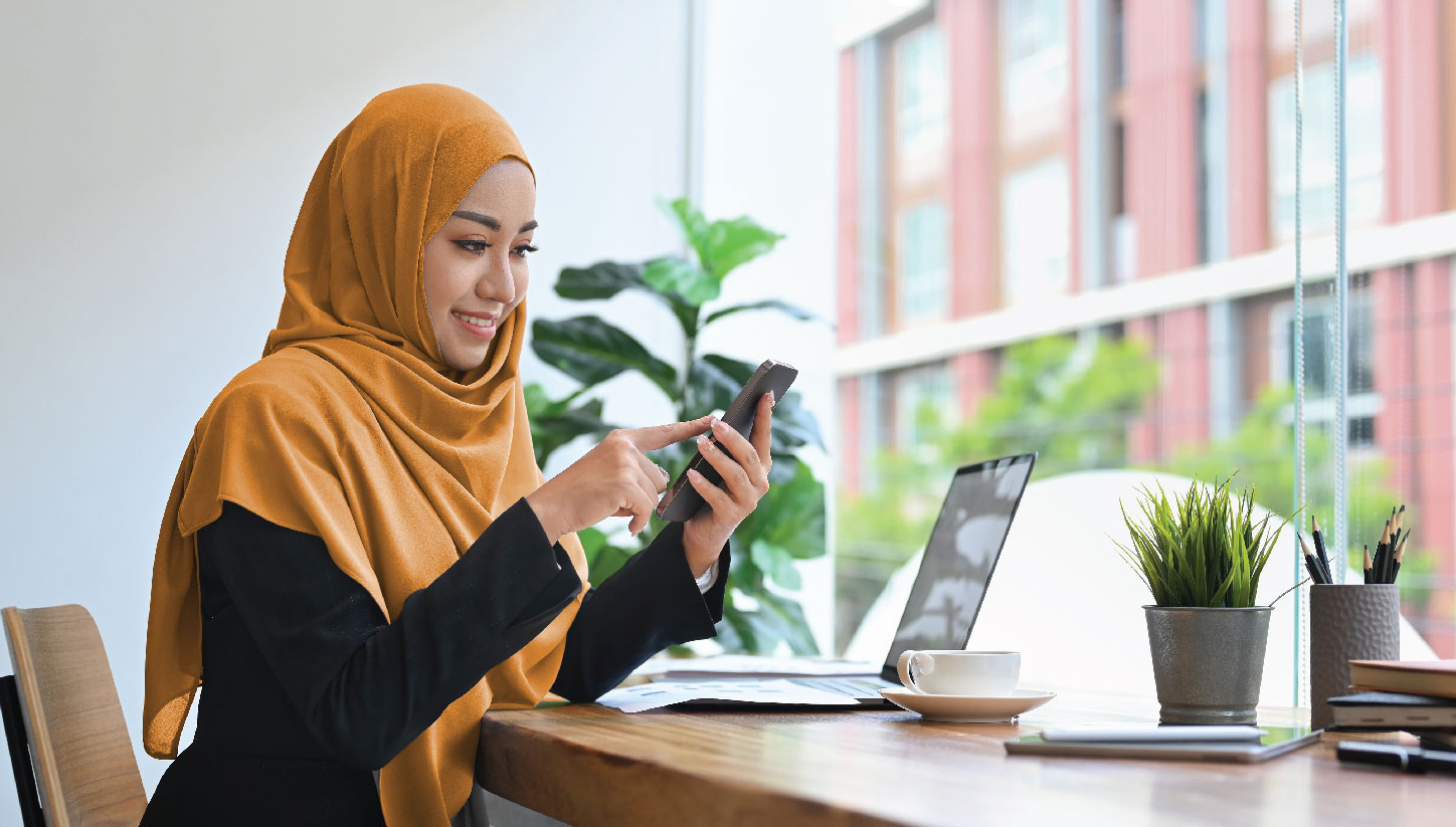 Woman in coffee shop window using phone and laptop