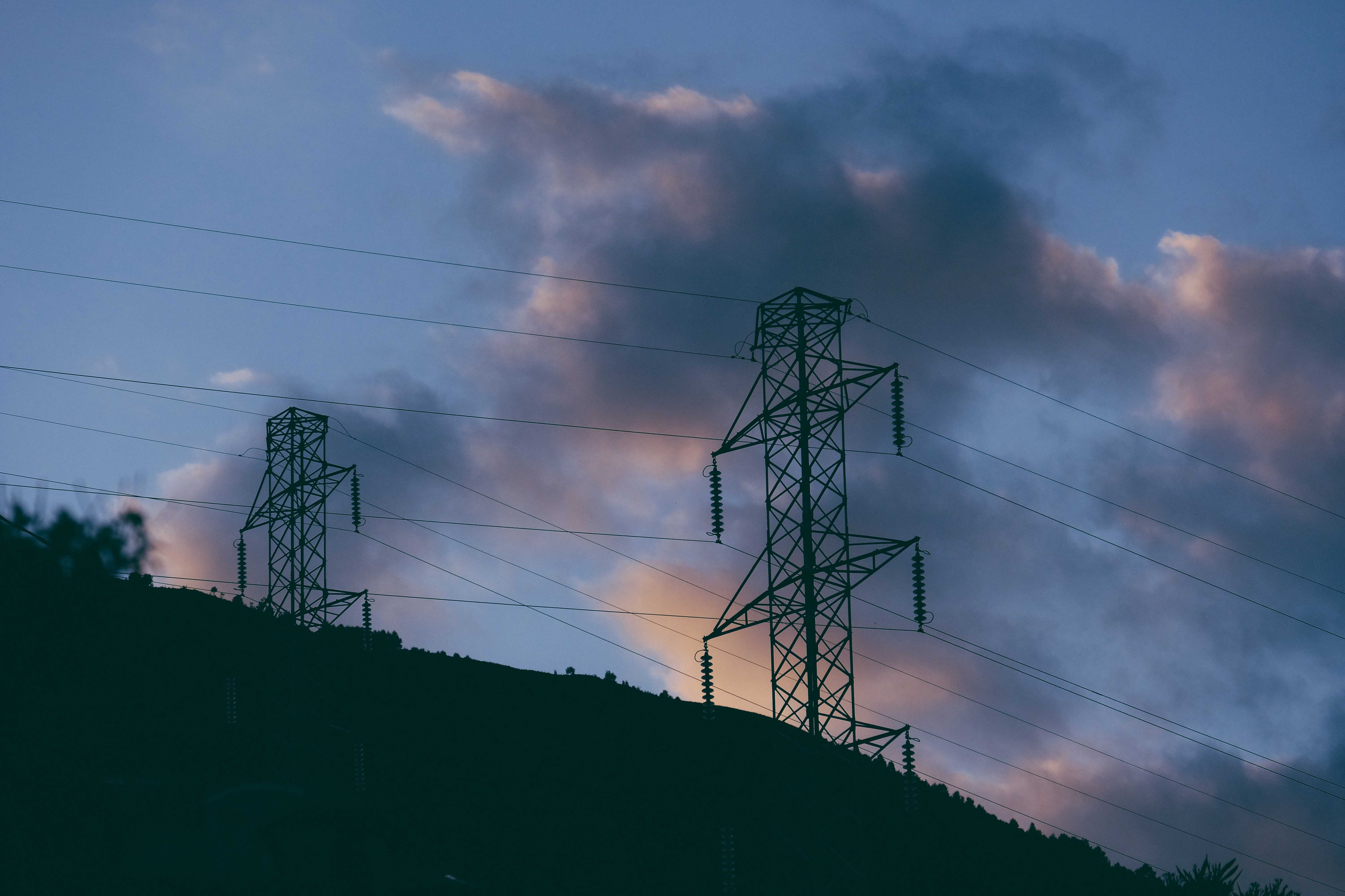 Electricity poles with cables located on hill at sundown