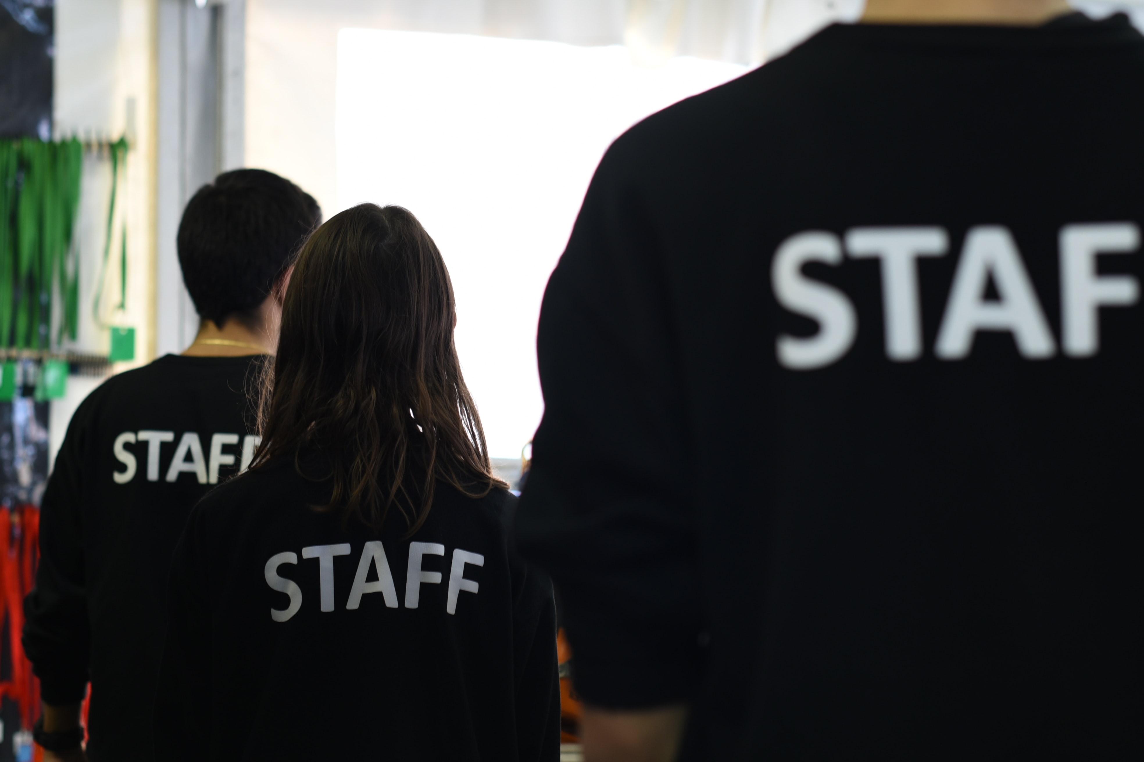 three workers photographed from the back wearing t-shirts with the words “STAFF" on tthem