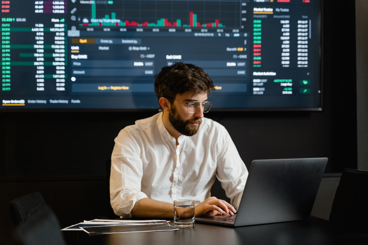 Man at laptop sitting in front of financial markets screen