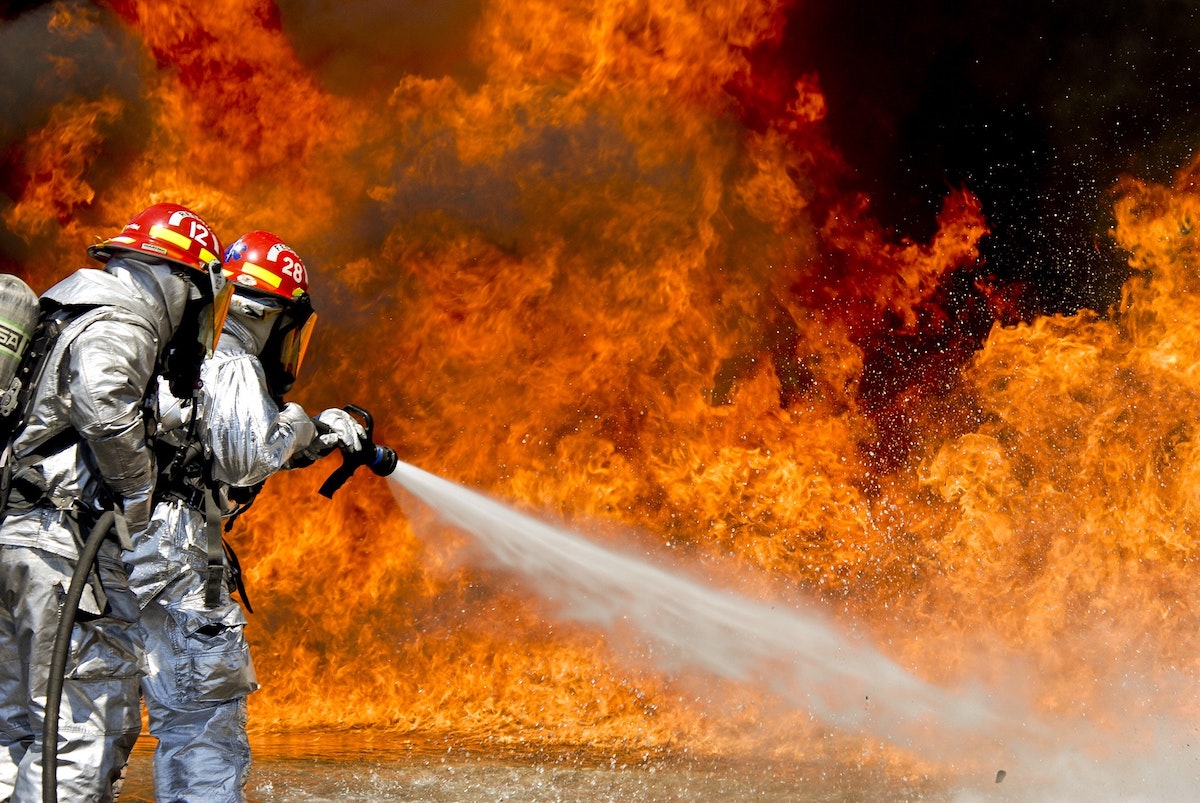 two firefighters holding on to a water hose and battling a big blaze