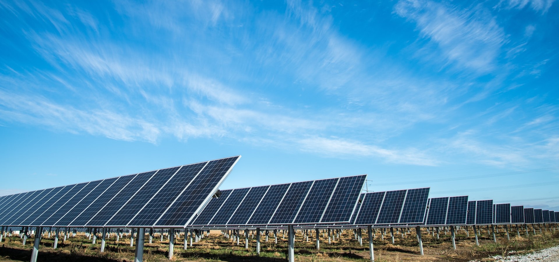Rows of solar panels on the ground pointing up to a cloudy blue sky