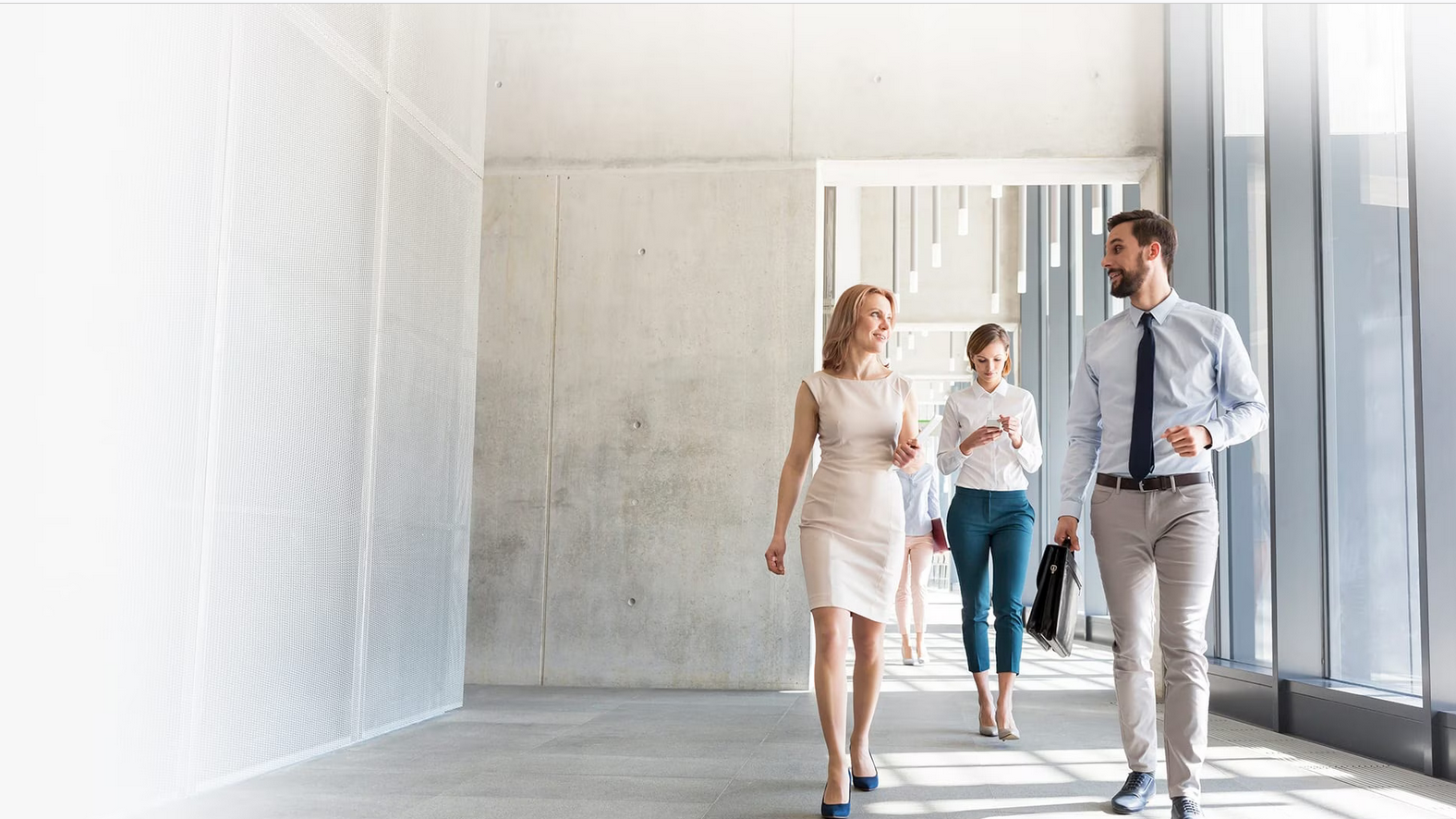 Two women and a man walk through a brightly lit concrete corridor