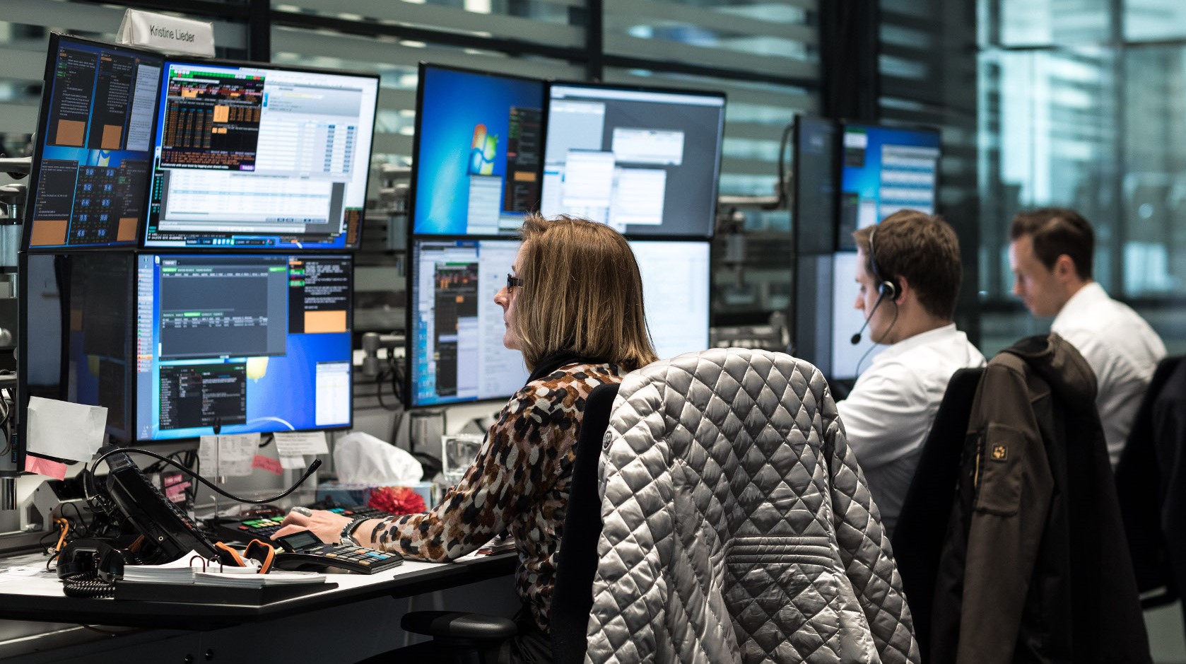 Three traders sitting at desks staring at multiple screens