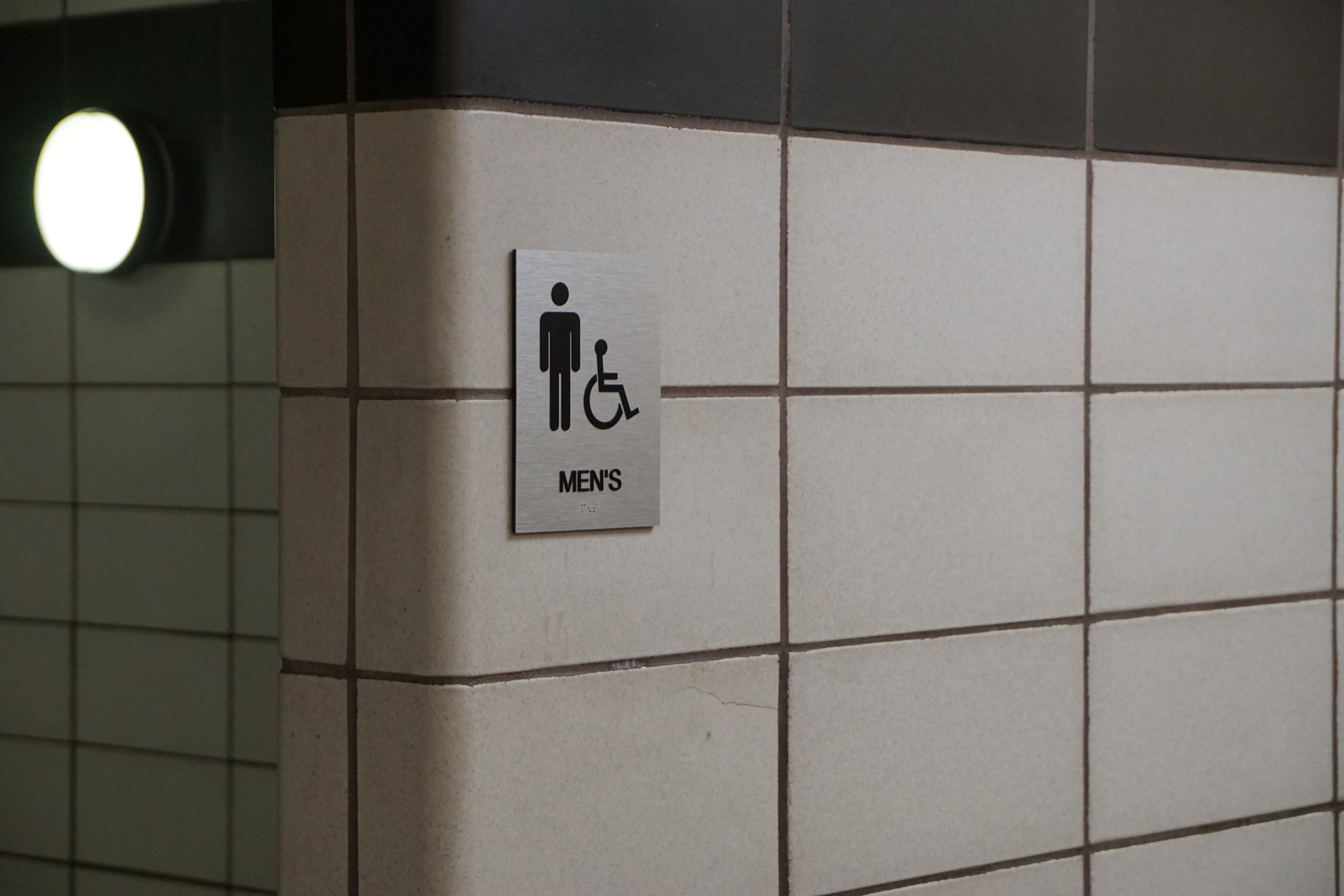 men's bathroom sign attached to a wall covered in white tiles