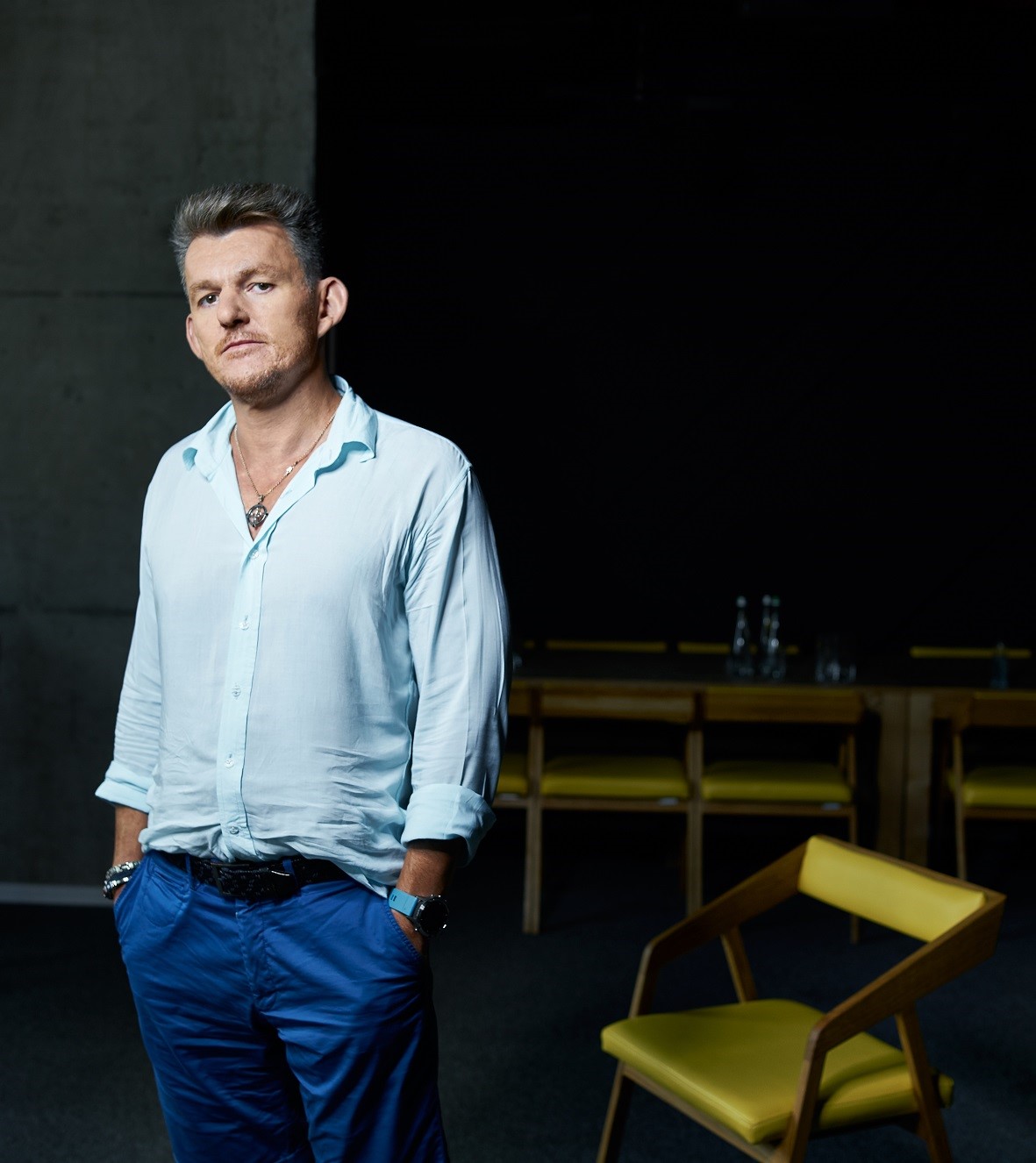 Dmytro Vartanian standing in a dark room next to a yellow chair