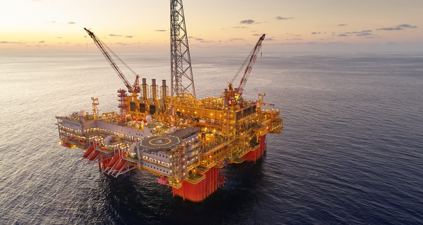 Gold, grey and red offshore oil rig in the middle of the ocean near sunset