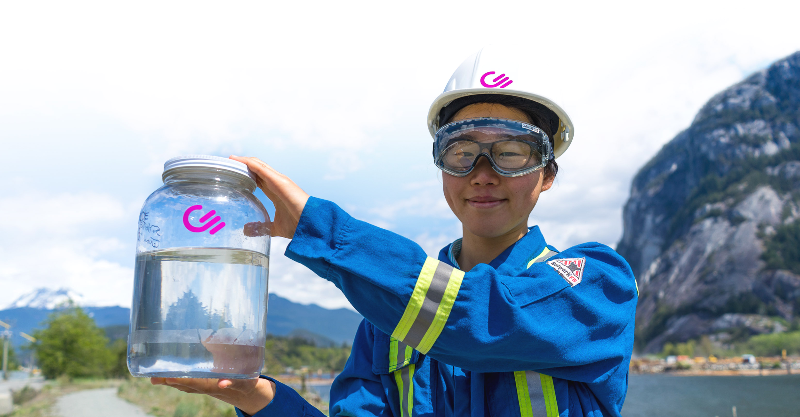 Woman in blue industrial suit holding up jar of liquid carbon
