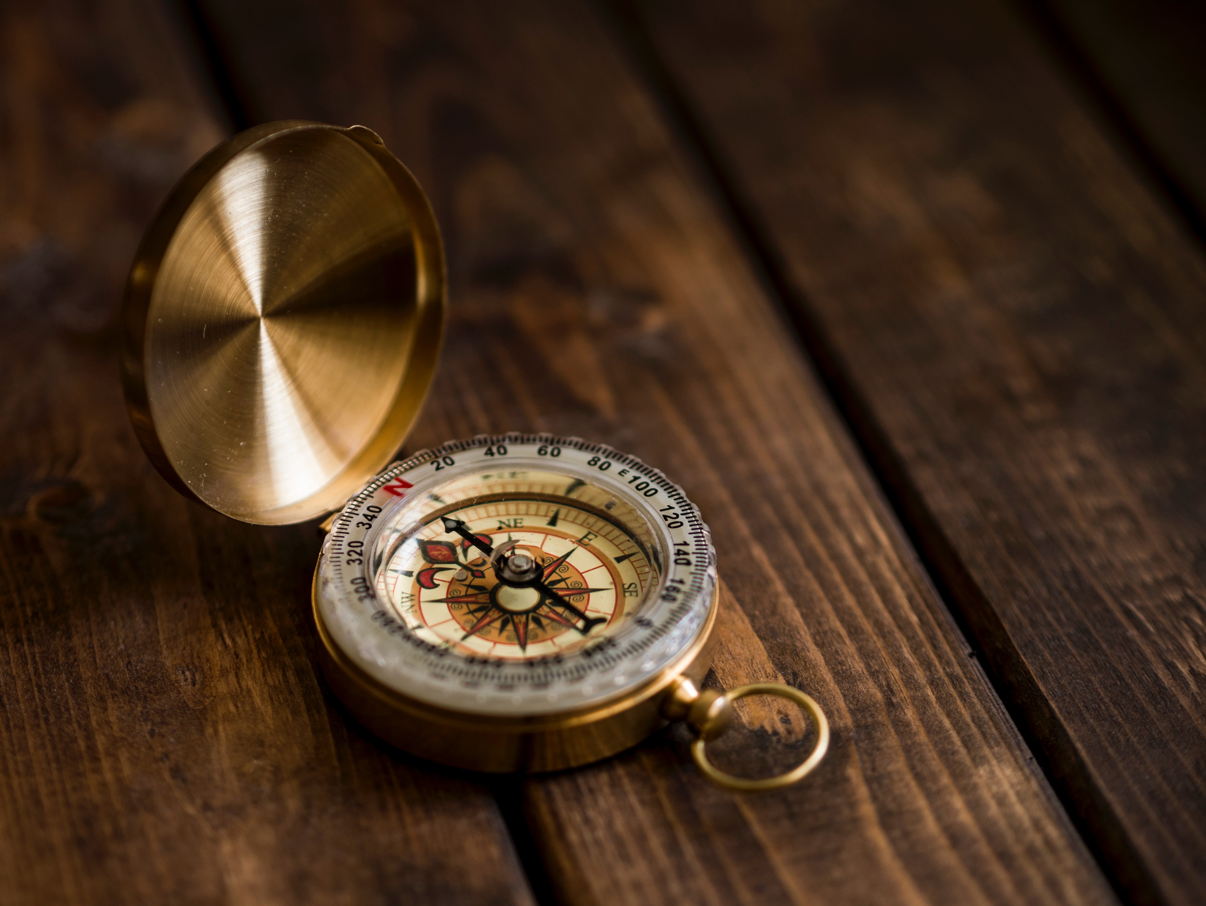 a golden, opened compass lying on a wooden table