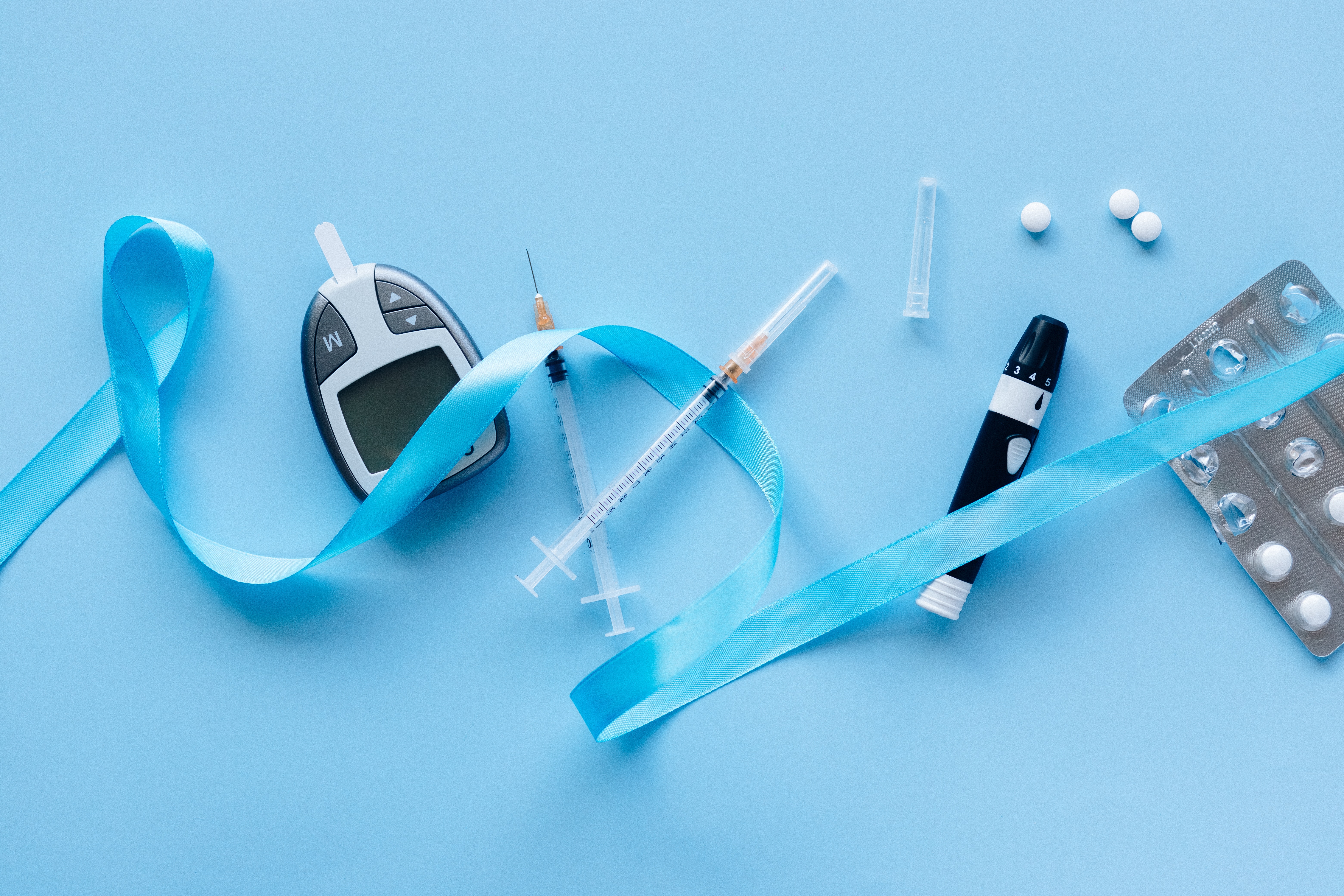 a continuous glucose monitor, syringes and pills lying on a blue table