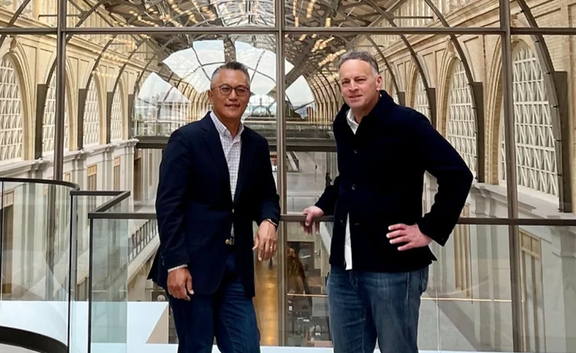 Jeff Herbst and Jay Eum of GFT Ventures lean against glass on the top floor of an arched building