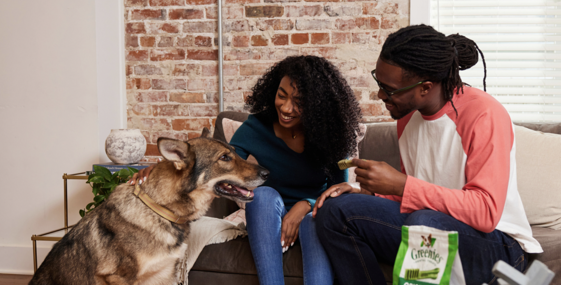 Man and woman on couch offer treat to dog