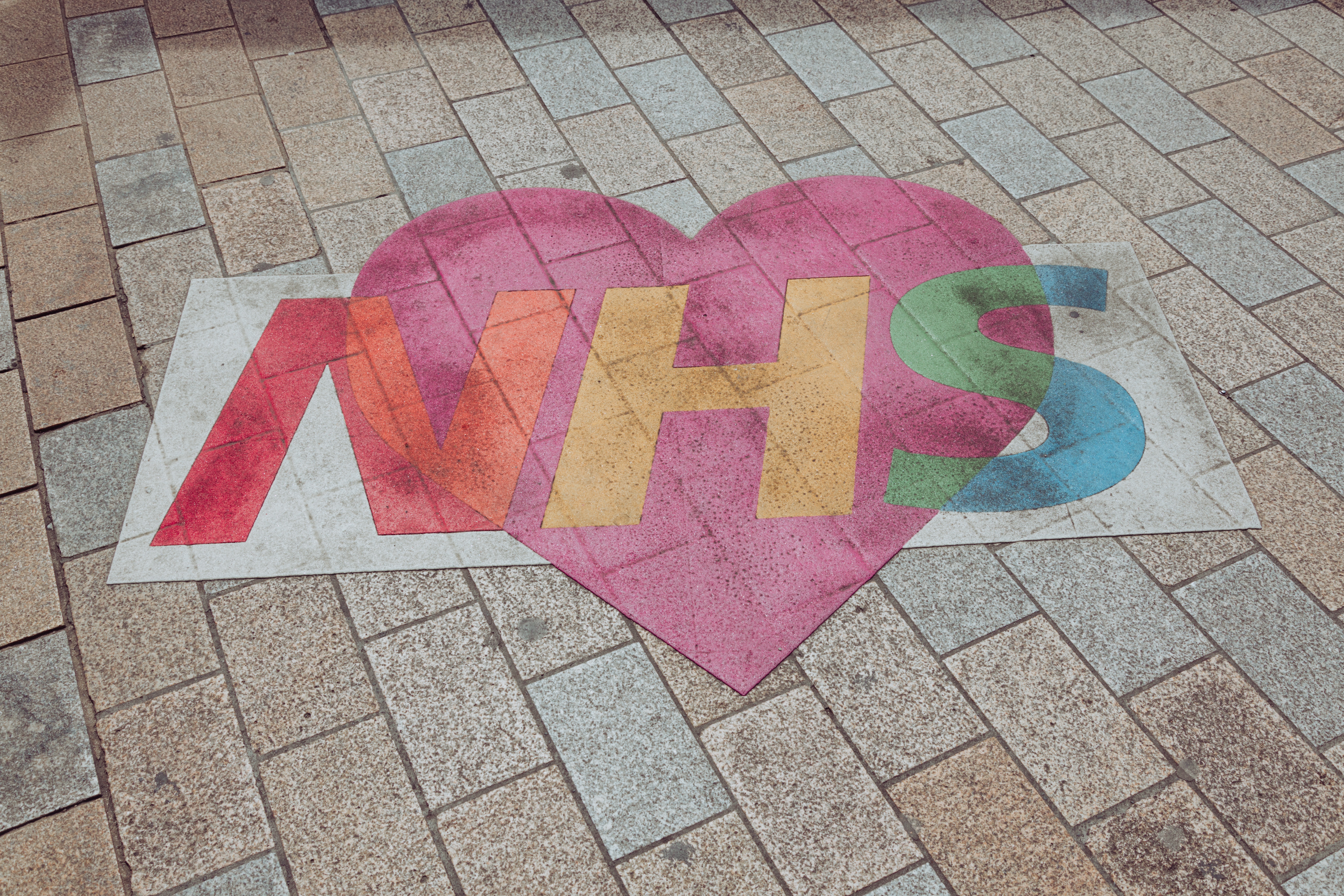 a chalk drawing on pavement of the NHS logo in rainbow colours with a pink heart in the background