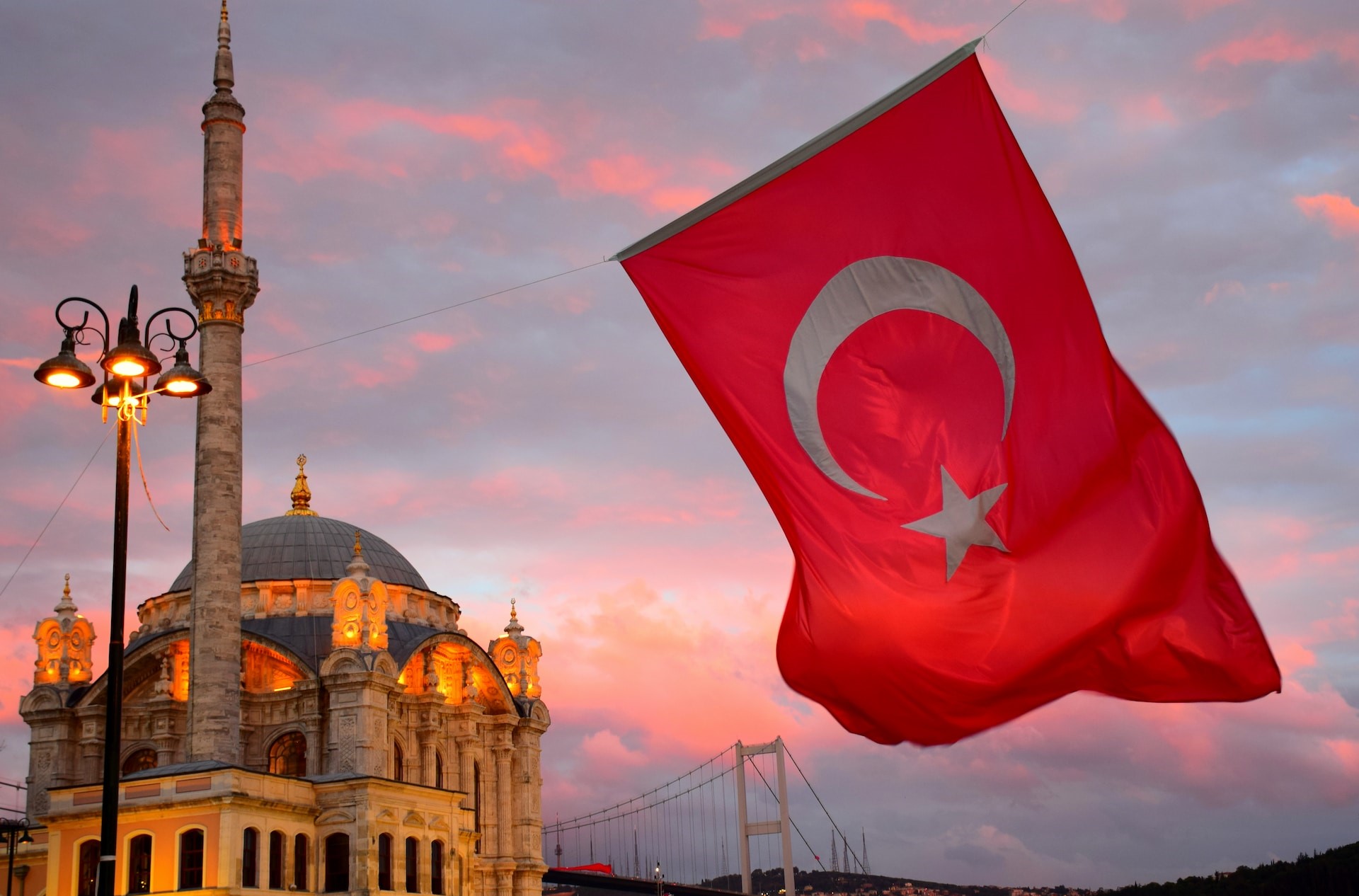 Turkish flag waves in front of a mosque at sunset with the Istanbul skyline in the background