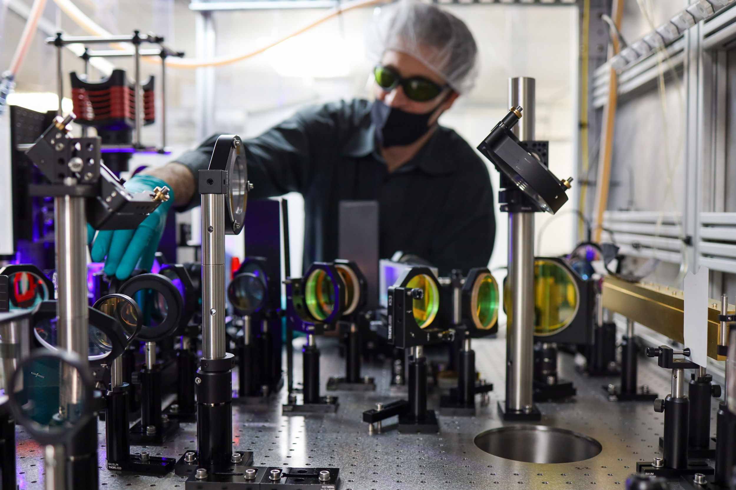 Man in goggles, face mask and hairnet jiggles with an assembly of coloured lenses.