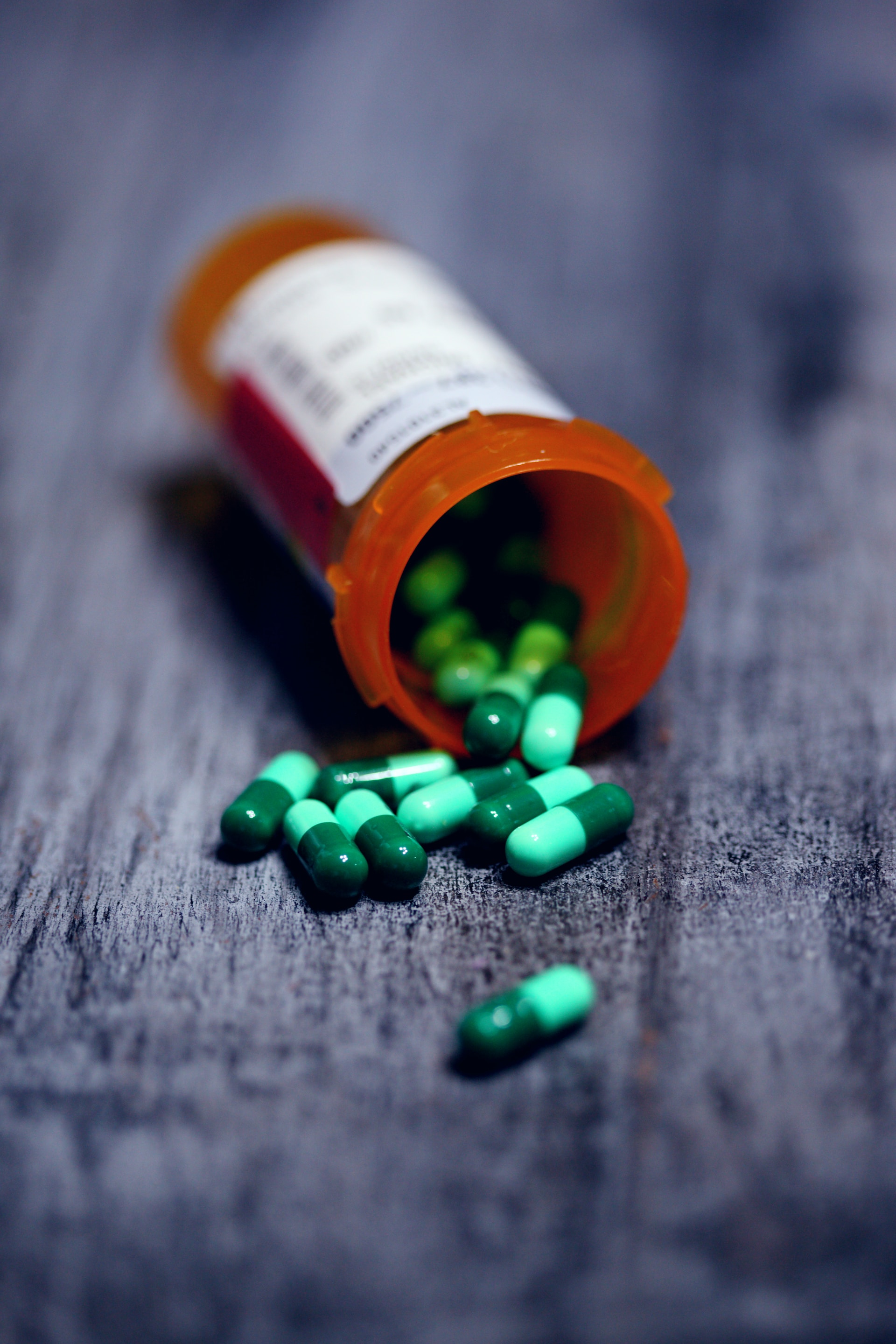 A pill bottle spills out green capsules on a grey carpet.