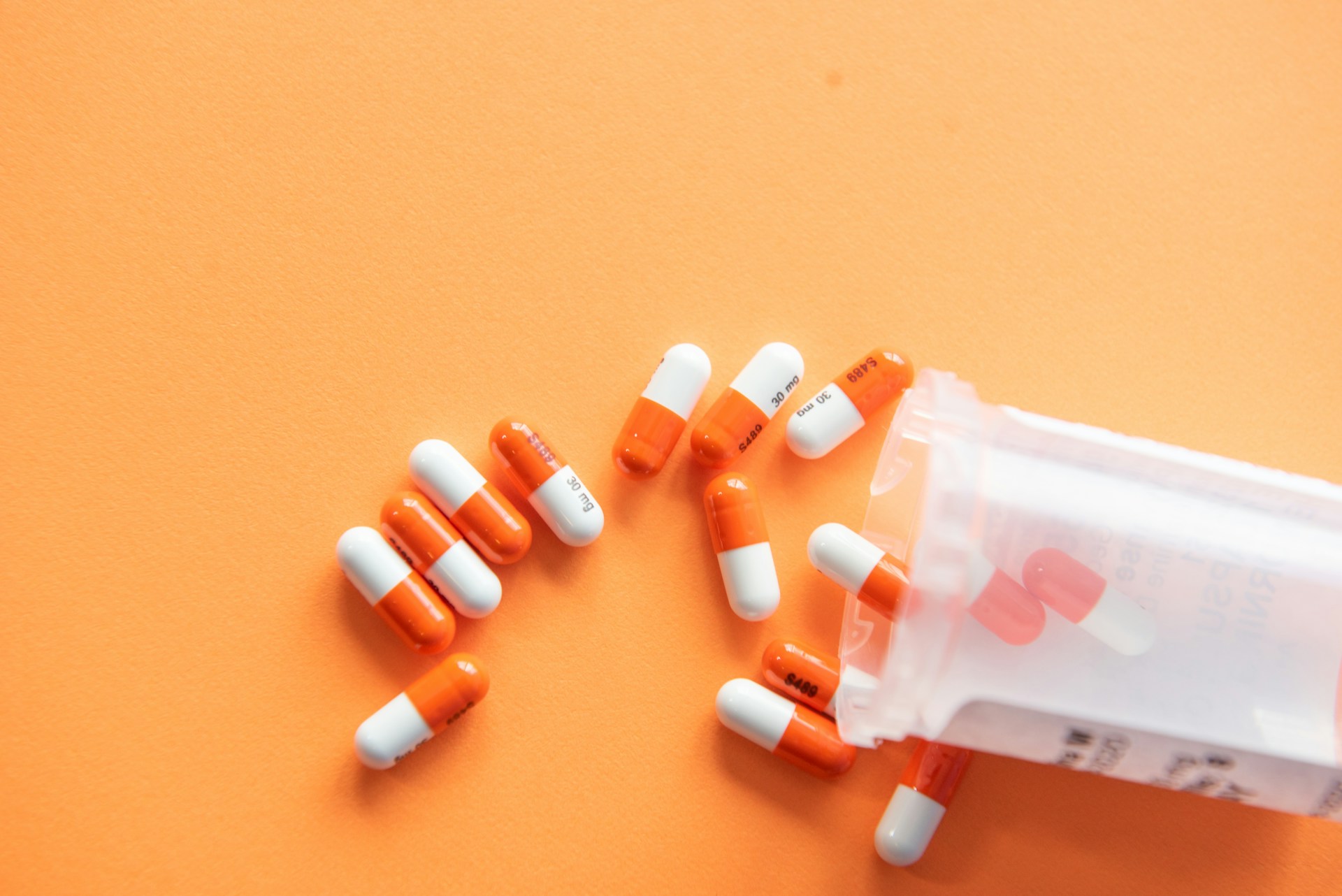 A pill bottle spills out orange and white capsules on an orange surface.