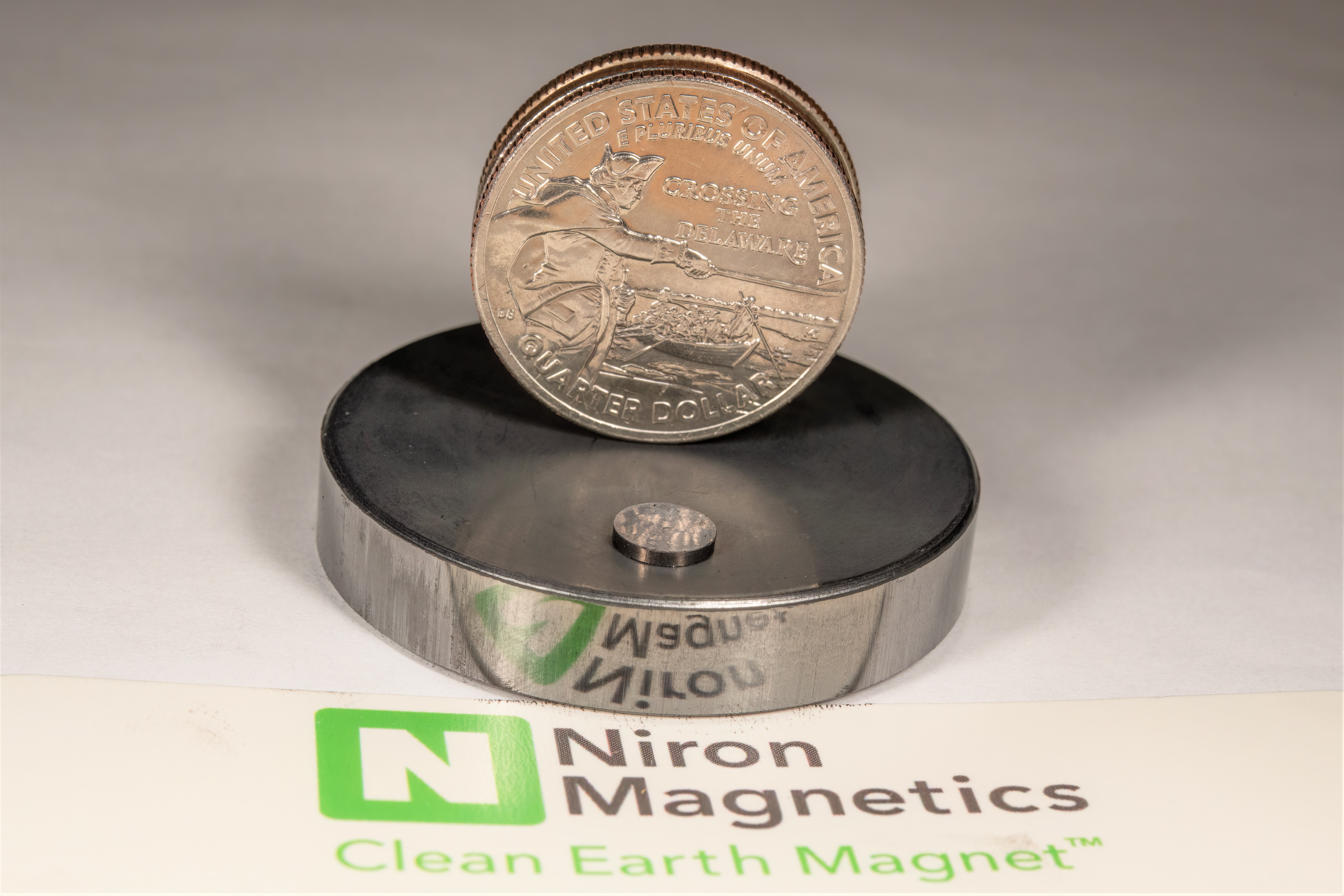 A coin and a small magnet balancing on a larger magnet, with Niron Magnetics' logo below.