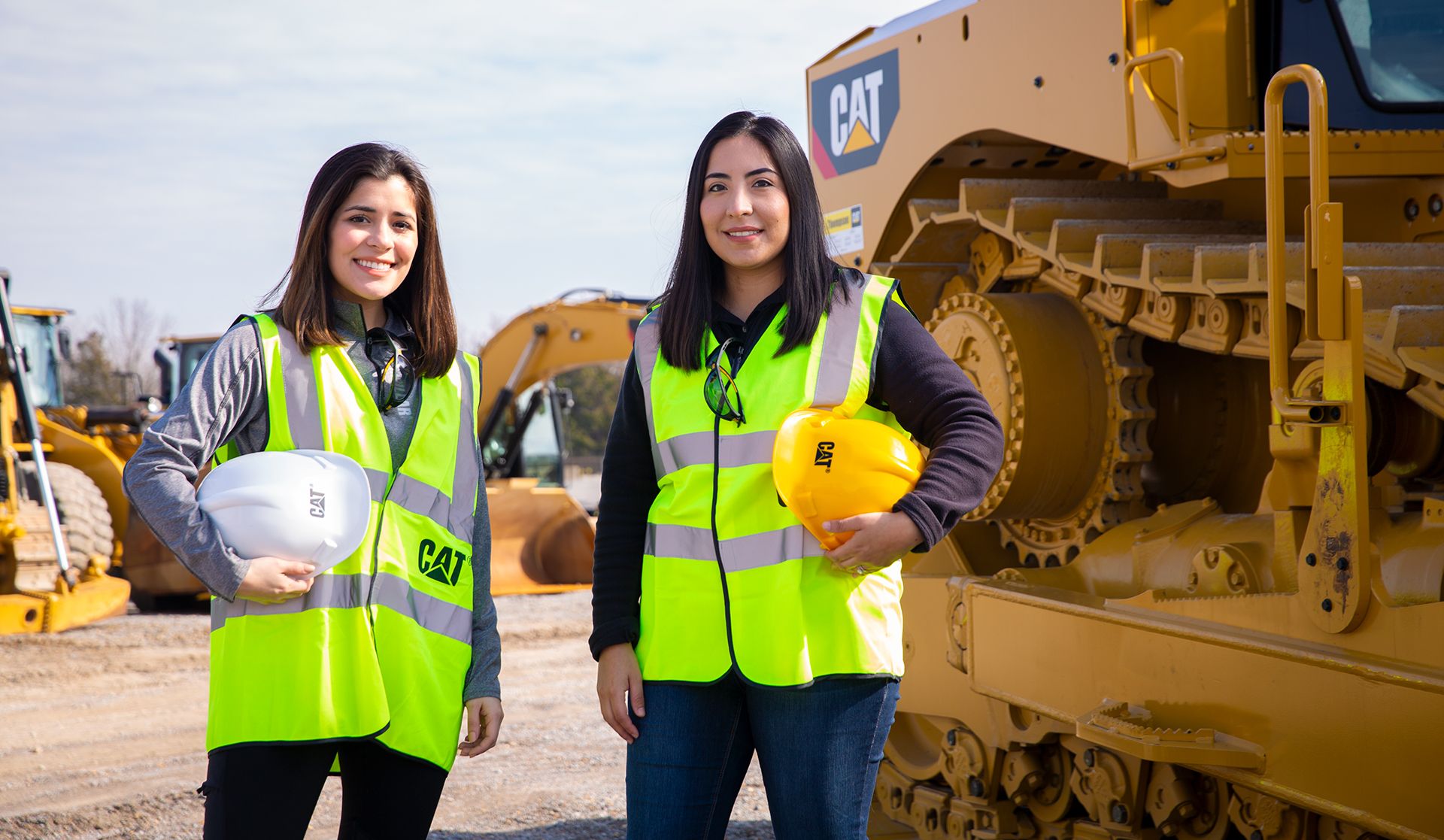 Two women in fluorescent workwear stand in front of construction machinery