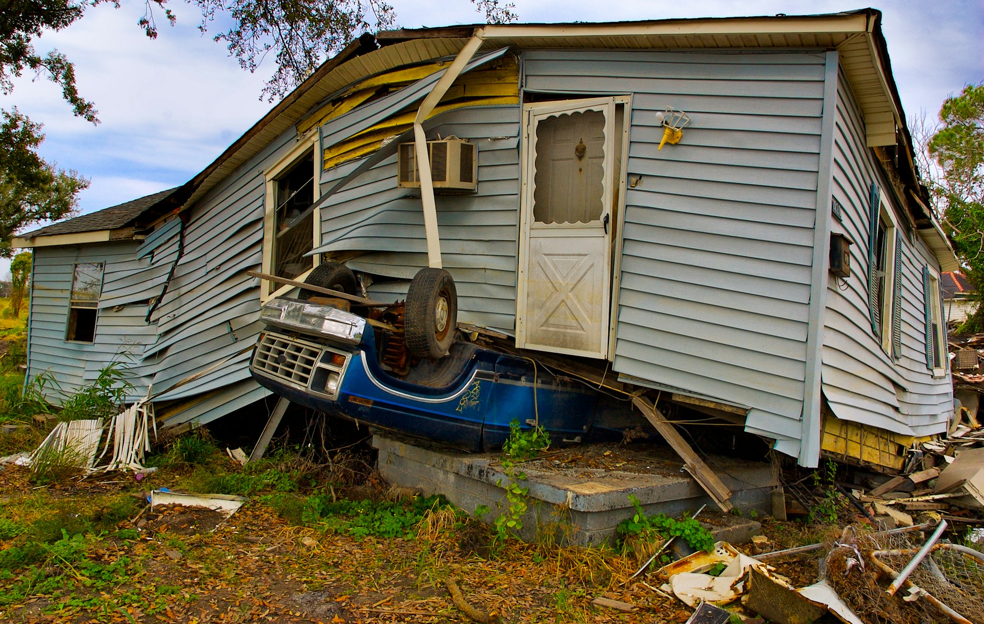 A hurricane ravaged one-floor house with an upturned pick up truck underneath it