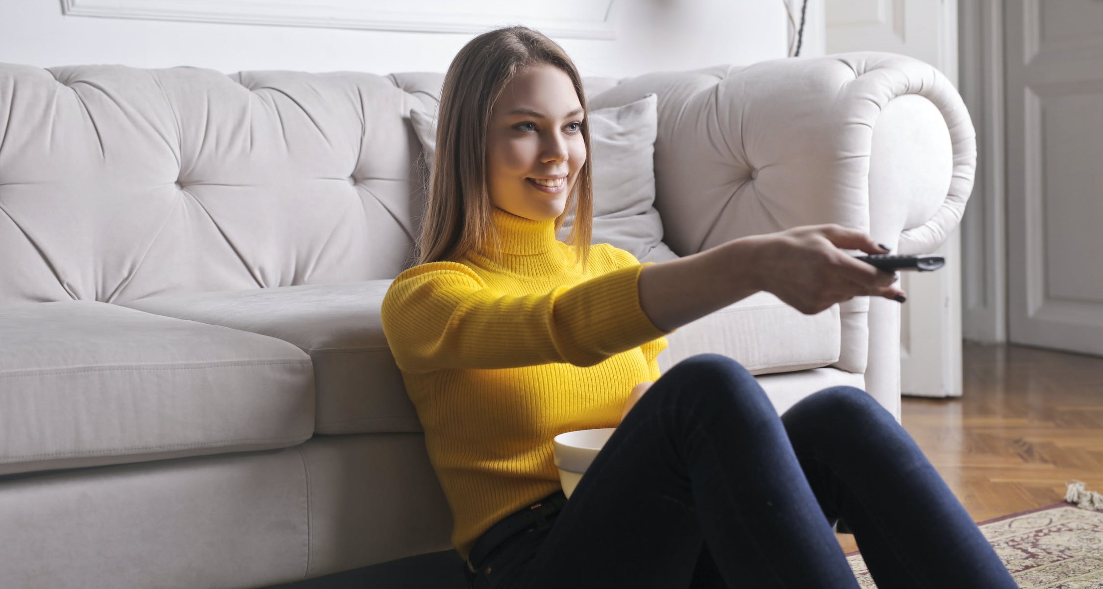 Woman sits in front of a sofa while pointing a remote control
