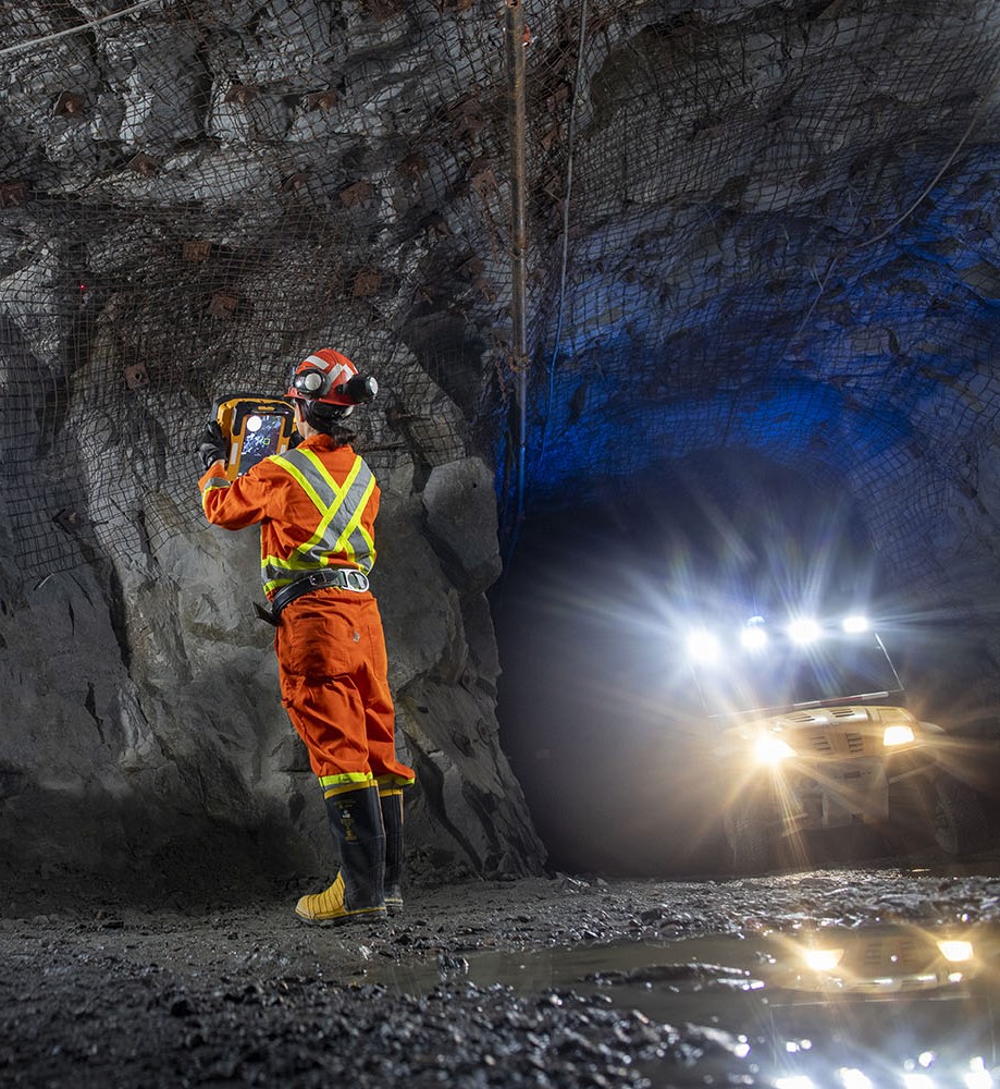 Miner using a RockMass device in an underground cave while a vehicle's headlamps shine 