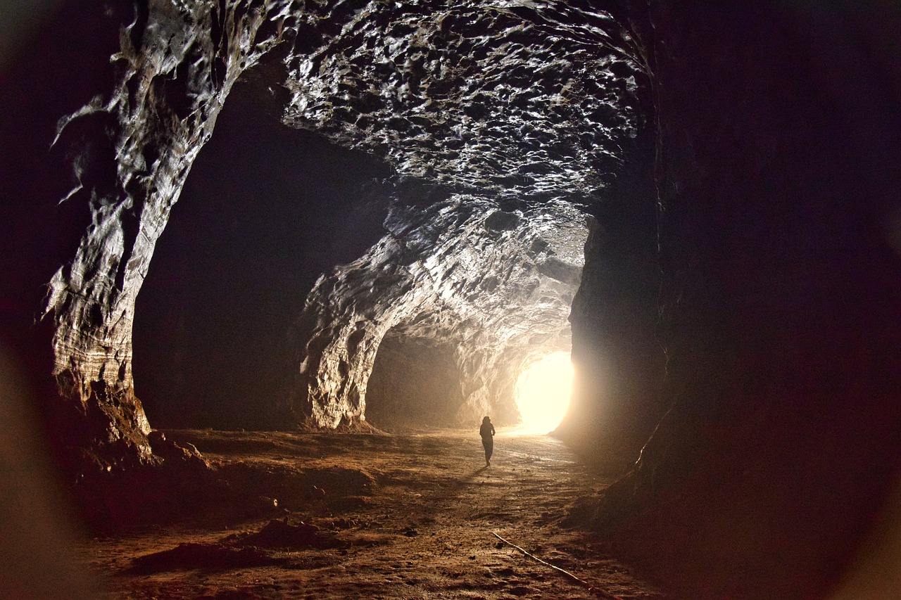 A person in silhouette walks through a cave towards the light.