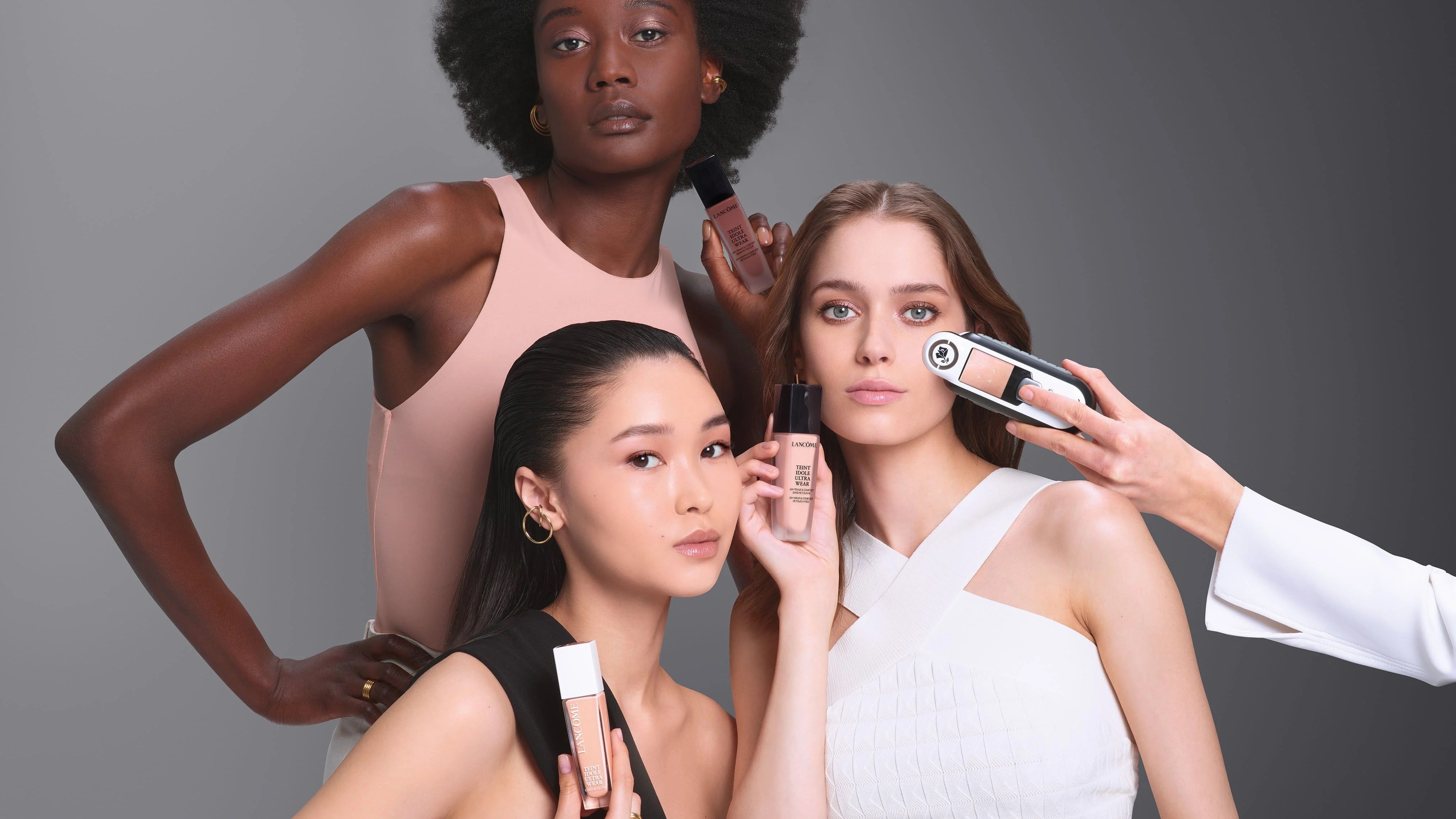 Three models with cosmetics products held up to their faces