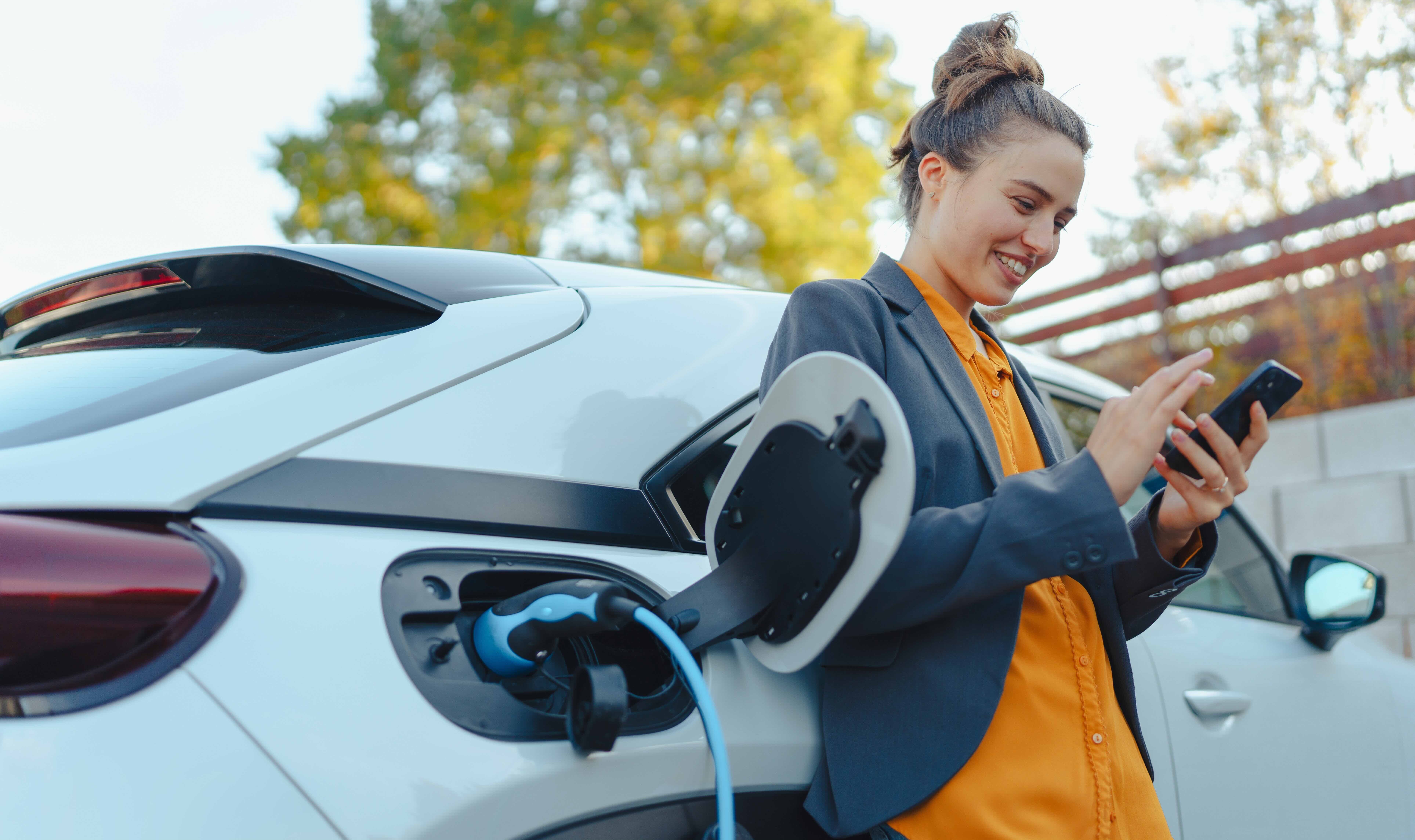 Young woman with smartphone waiting while her electric car is charging 