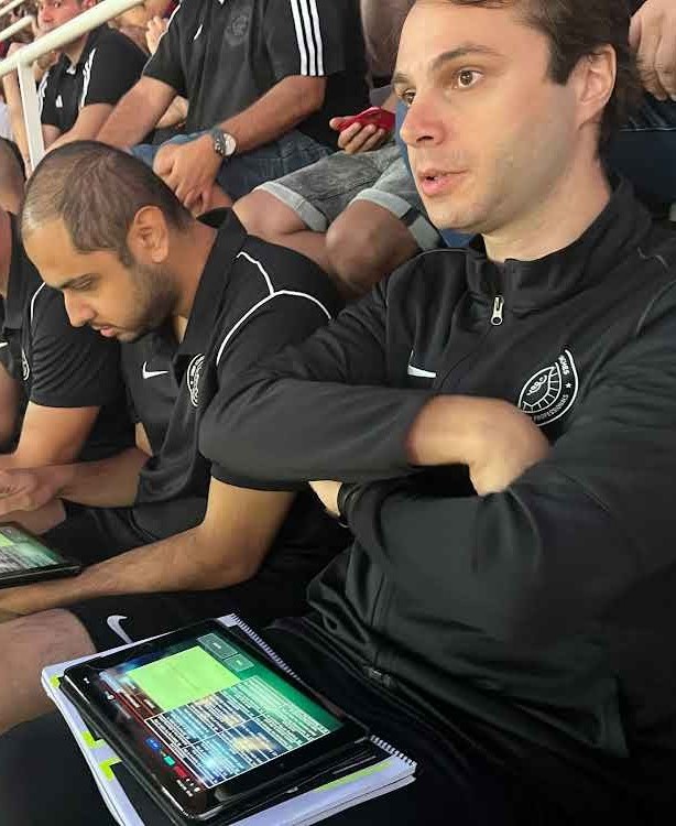 Two analysts with tablets sit watching sport