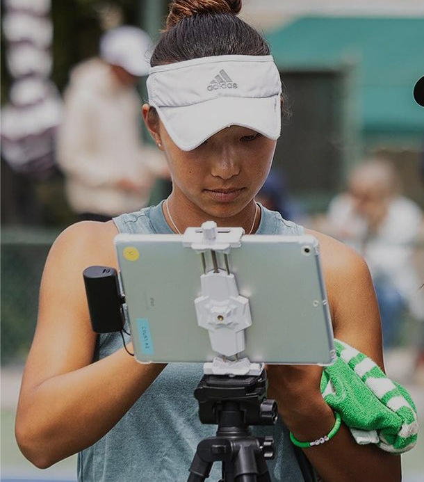 A tennis player looks at a mounted tablet screen during a break in her match