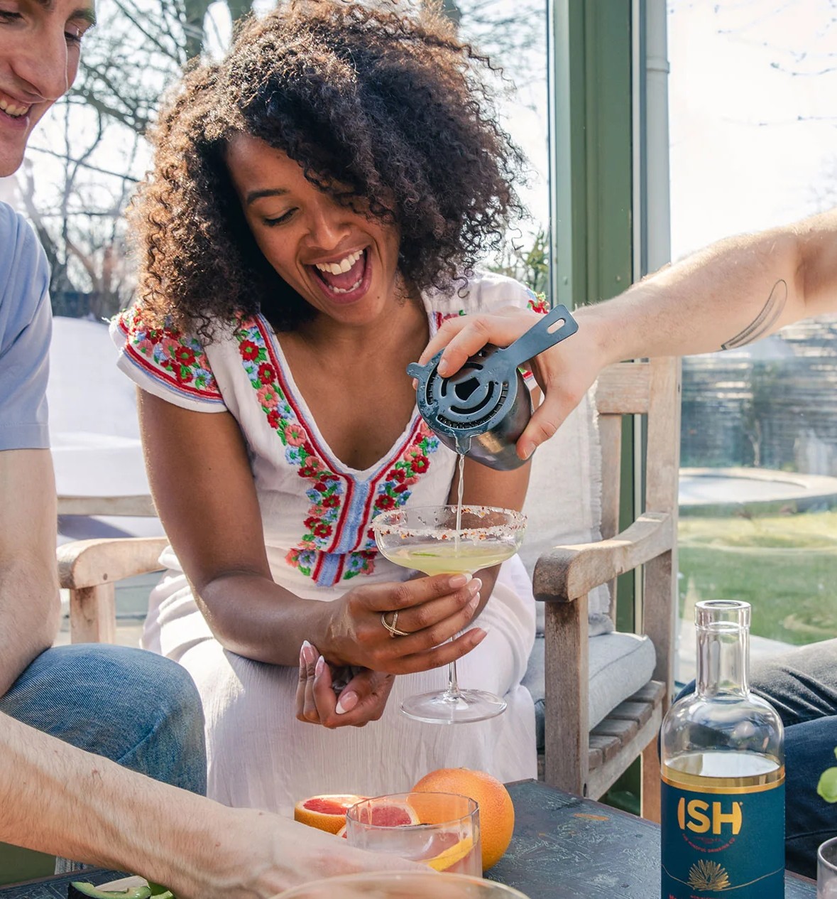 A woman laughing as someone pours some ISH into her martini glass