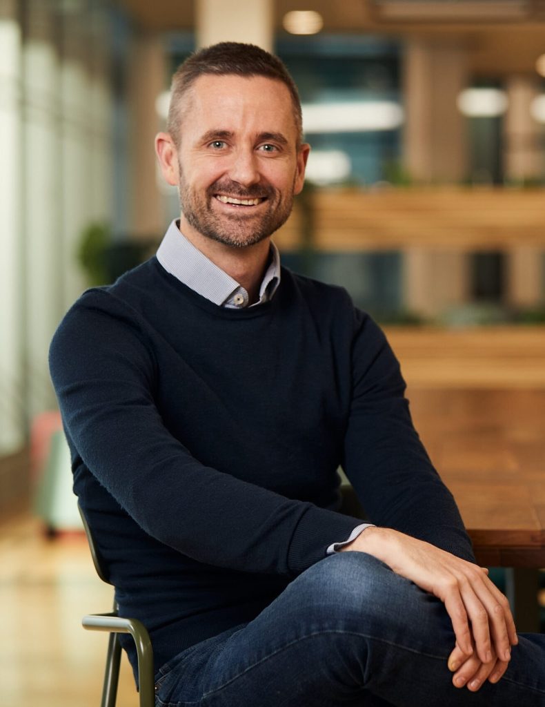 Brendan Kilcawley in a jumper sitting with his hand on his knee